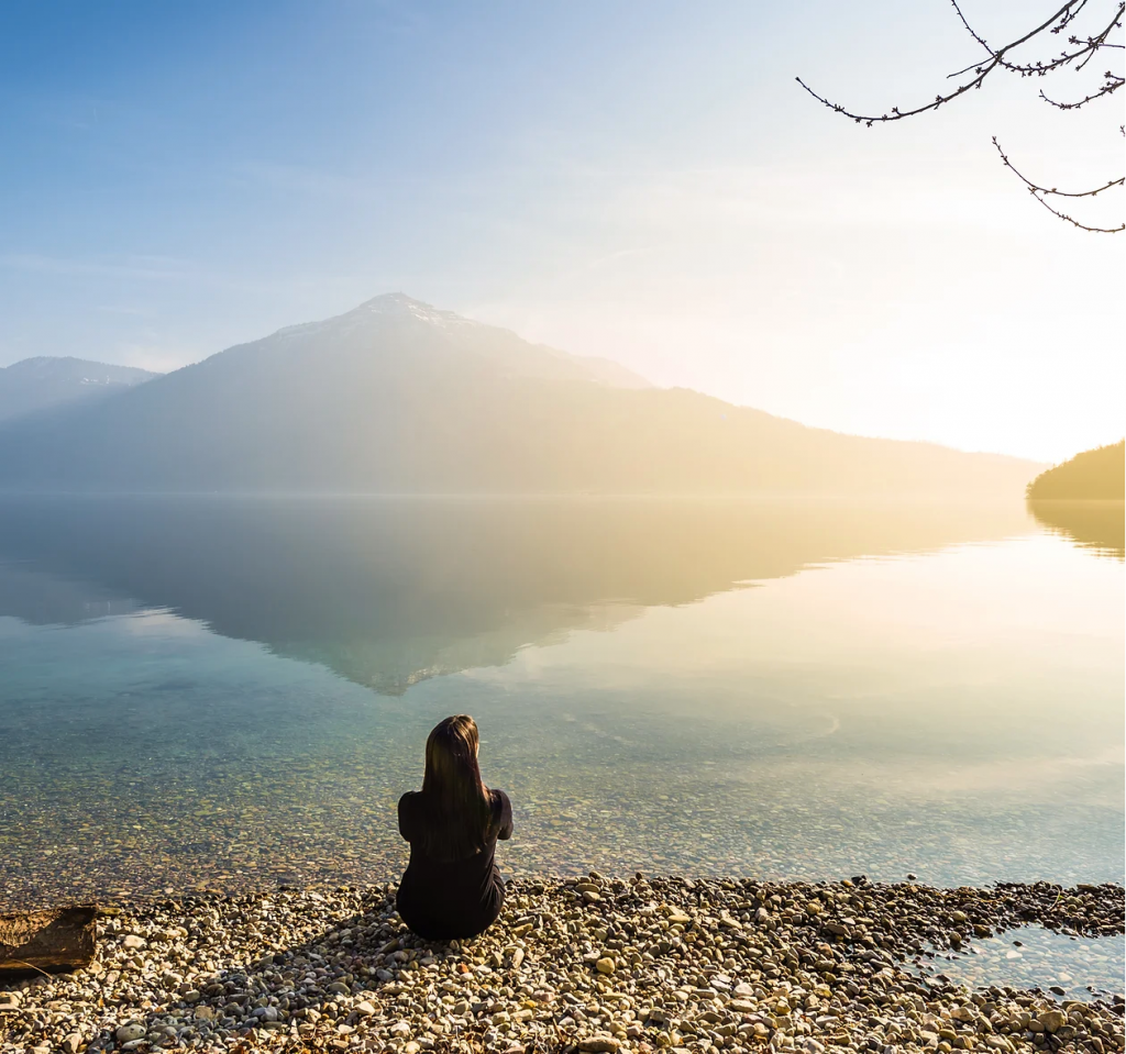Woman sitting on a rocky beach overlooking a lake and mountains